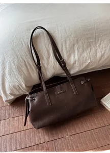 Detailed view of deep brown faux leather tote bag with metal logo on elegant wood floor