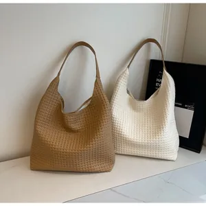 Detail of khaki and beige woven tote bags with wide leather handles on marble surface