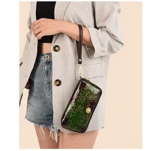 Detailed view of green retro wristlet bag with floral embossing and brown strap