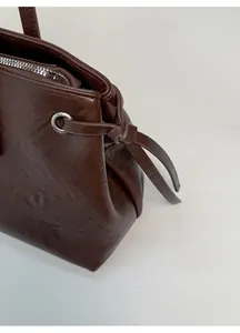 Detail of dark brown leather tote featuring side drawstring knots and silver metal zipper