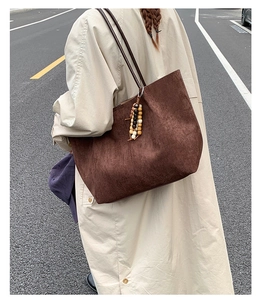 Detail of a large dark brown tote bag with suede texture and wooden bead charm on shoulder