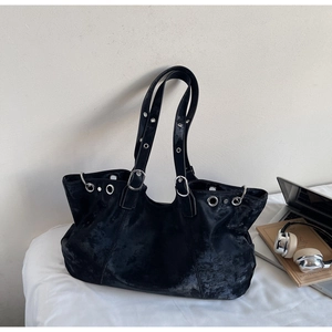 Detail der schwarzen Shopper-Tasche mit Vintage-Textur und silbernen Ösen auf weißem Bett