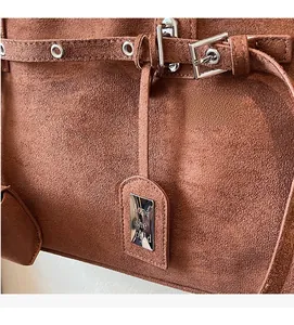 Detail of brown suede shoulder bag featuring silver buckle and decorative metal tag