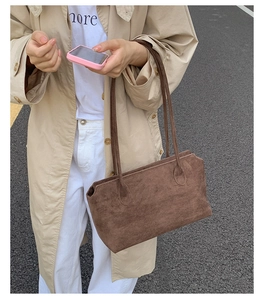 Brown suede tote bag on shoulder of model in trench coat against asphalt road background