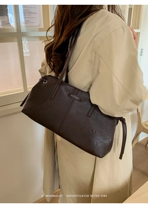 Detail of a dark brown vintage leather handbag with a metal logo on a beige trench coat