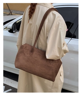 Brown suede tote bag worn over the shoulder with beige coat in an outdoor urban setting