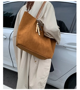 Detailed side view of a large brown matte tote bag with beaded charm on a shoulder strap