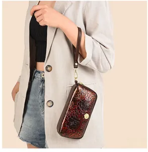 Detailed view of a dark brown floral embossed wristlet bag held by a model