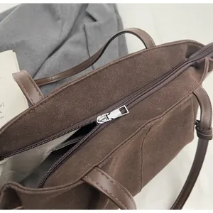 Detail shot of the silver metal zipper and smooth leather strap on a brown suede tote bag
