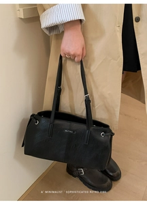 Detail of minimalist black leather tote bag featuring a brand logo and side drawstring
