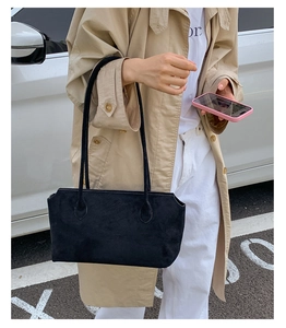 Outdoor shot of a black matte suede shoulder bag paired with a classic trench coat