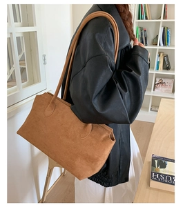 Detailed side view of brown suede tote bag worn on shoulder in a modern room setting