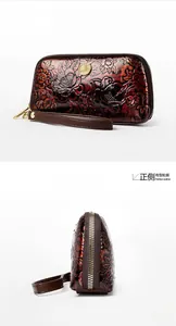 Detail view of red-brown floral embossed leather wallet with metal zipper and wrist strap