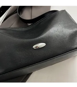 Close-up of black matte leather shoulder bag featuring a silver oval metal hardware detail