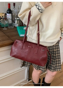Detail of burgundy leather tote bag with pleat texture and MUTING logo shown on shoulder