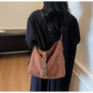 Detail of red-brown suede tote bag with decorative strap and silver metal rings