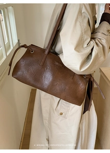 Close-up of brown vintage leather shoulder bag with logo on a beige trench coat