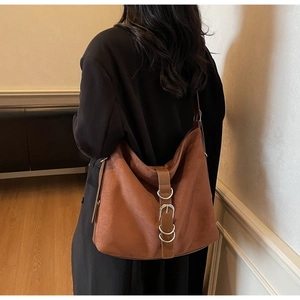 Close-up of large brown suede tote bag featuring metallic rings and buckle details