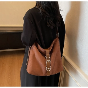 Close-up of brown suede tote bag with metal buckles and decorative rings on shoulder strap