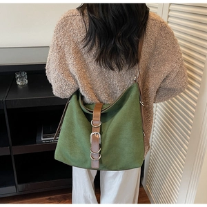 Detail of green canvas tote bag with brown leather straps and silver buckle accents