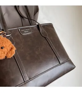 Detail of dark brown tote bag with white stitching, litchi texture and dog charm
