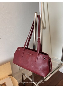 Close-up of a burgundy leather tote bag featuring a magnetic silver buckle and MUTING logo