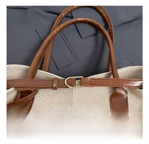 Detail of golden D-ring hardware on beige woven canvas tote bag with brown leather strap