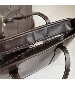 Close-up of smooth metal zipper and reinforced stitching on dark brown leather tote
