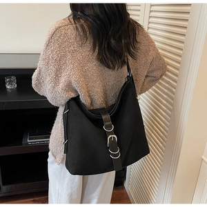 Detail view of large black matte suede tote bag with bold silver metal buckle on shoulder