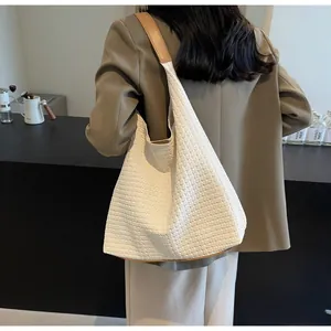 Close-up of white woven tote bag with brown leather straps shown on model shoulder