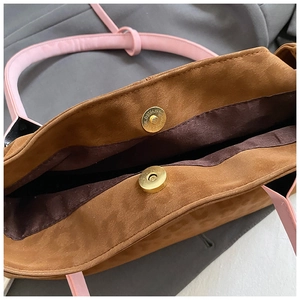 Detail of the golden magnetic buckle and pink strap on this brown suede tote bag