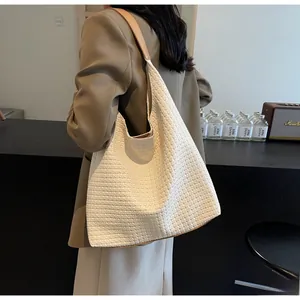 Detail of a large woven hobo tote bag with brown leather handles worn by a model