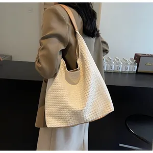 Detail of woven cream tote bag showing fine texture and brown leather shoulder strap