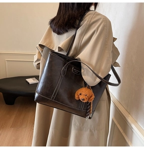 Detailed side view of deep brown leather tote bag with white stitching and plush charm