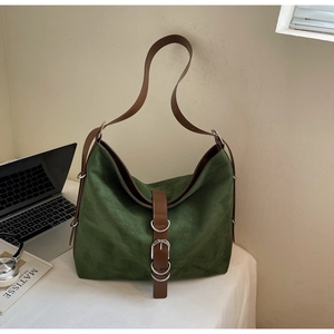 Close-up of dark green suede tote bag with brown leather straps on a white desk
