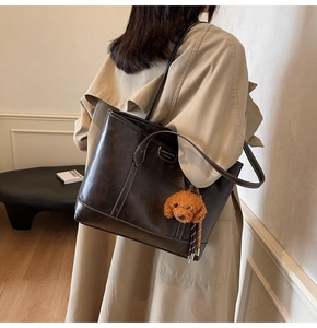 Detail view of large brown leather tote bag with white stitching and teddy bear charm