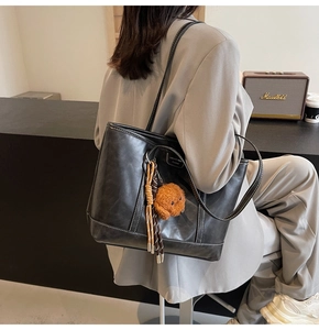 Detail of black leather tote bag with white contrast stitching and teddy charm