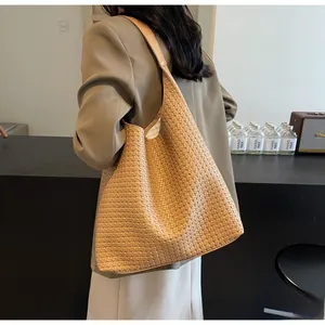 Brown woven tote bag shown on model shoulder in a professional indoor fashion setting