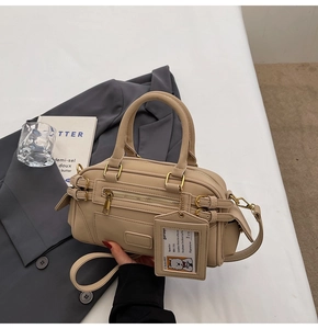 Detail of beige Boston bag with metallic buckles and decorative tag on gray blazer