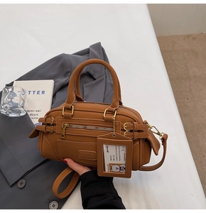 Detailed view of brown faux leather Boston bag with decorative straps and creative ID card charm