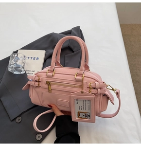 Detail of pink matte PU leather Boston bag with dog tag charm on a chic blazer background