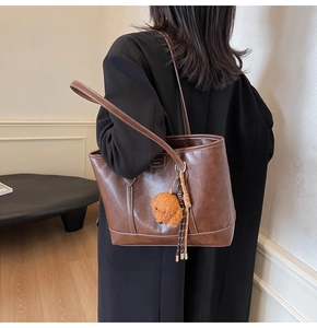 Detailed view of brown leather tote bag featuring contrast white stitching and puppy charm