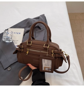Detailed view of brown Boston bag with metal buckles and dog tag in a lifestyle setting