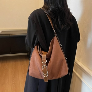 Brown faux suede crescent tote bag with decorative silver rings worn by a model