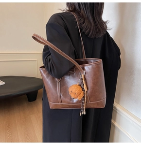 Brown leather tote bag featuring contrast stitching and a cute teddy bear charm detail