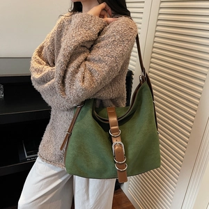 Green suede tote bag with brown leather strap and silver metal buckle in a home setting