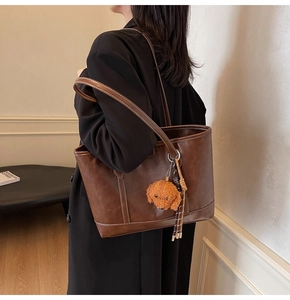 Close-up of vintage brown tote bag with white stitching and plush puppy pendant