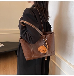 Detail of vintage brown leather tote bag with white contrast stitching and teddy charm