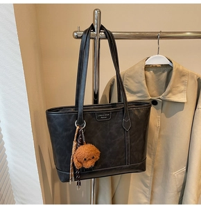 Detail of black tote bag with white contrast stitching and a brown teddy bear pendant
