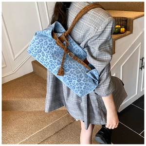 Detail of blue leopard print tote bag featuring brown leather straps and side buckle accents